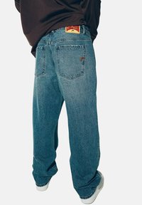 Niebieskie dżinsy w luźnym fasonie, z czerwoną i żółtą naszywką marki na tylnym pasku oraz dwoma tylnymi kieszeniami.