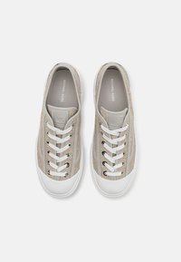 Beige tekstilsko sneakers med hvite gummi såler, med snøring foran, teksturert overdel og en logo-plakett på tungen.