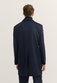 Marineblauer Wollmischmantel mit klassischem Schnitt, ausgestattet mit einem Rückenschlitz und taillierten Ärmeln, glatter Textur und dezentem Glanz.