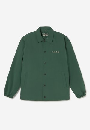 Giacca verde scuro con bottoni, polsini elasticizzati, due tasche laterali e scritta bianca "Kustka Society" sul petto sinistro.