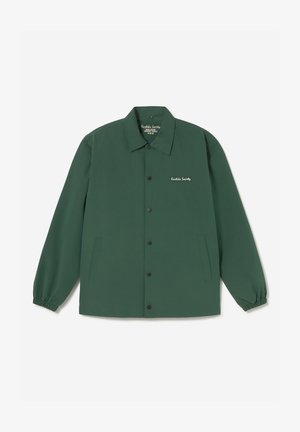 Veste boutonnée vert foncé avec poignets élastiques, deux poches latérales et texte blanc "Kustka Society" sur la poitrine gauche.