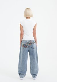 White fitted t-shirt with cap sleeves paired with loose, light blue denim jeans featuring colorful embroidered design on the back pockets.