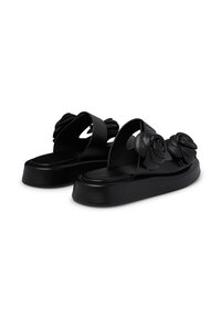 Black platform sandals featuring sculpted flower accents, made from smooth leather, with open sides and a rounded toe design.