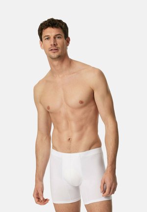 Boxers en coton blanc avec une taille élastique, présentant une texture lisse et un ajustement confortable, portés par un modèle masculin debout.