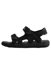 La sandalia negra presenta dos correas de Velcro, una plantilla texturizada y una suela de goma flexible con patrones de tracción. Diseñada para la comodidad y el soporte.