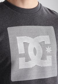 Šedé bavlněné tričko s bílou grafikou a horizontálními proužky a logem ve středu, kulatý výstřih, minimální textura.