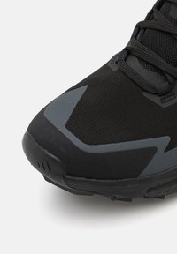 Scarpa sportiva nera con tomaia texturizzata, dettagli grigi e punta rinforzata. La suola è in gomma con un robusto motivo di grip.