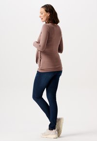 Brun langærmet top med sidelægning, parret med mørkeblå skinny jeans og lysegrå sneakers. Glat stof og tætsiddende design.