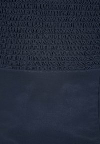 Mörknavy tyg med texturerad smockning i den övre delen och en slät yta nedanför. Inga ytterligare mönster eller detaljer synliga.