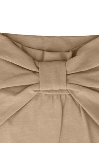 Haut en tissu beige avec un grand nœud à l'avant, fabriqué à partir d'un matériau texturé doux, présentant des accents plissés en dessous du nœud.