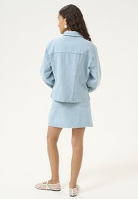 Giacca di jeans blu chiaro con vestibilità rilassata, abbinata a una gonna coordinata. Tessuto liscio, orlo curvo e design informale. Bottoni trasparenti e tasche.