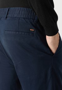 Navy blue trousers with a smooth texture, elastic waistband, side pockets, and a subtle back pocket featuring a small BOSS logo.