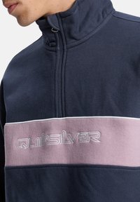 Marinefarbener Fleece-Pullover mit halbem Reißverschluss und pinkem Streifen. Mit gesticktem "Quiksilver", hohem Kragen und weichem Material.