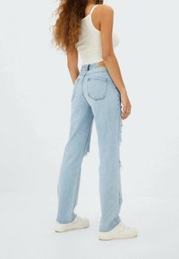 Ljust blå rivna jeans med rak benpassform, utrustade med två bakfickor och ofärdiga fållar. Matchas med vita sneakers och en vit topp.