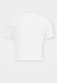 Camiseta blanca, recortada, hecha de tela acanalada con mangas cortas, un escote redondo y un pequeño parche en la parte posterior como detalle de diseño.