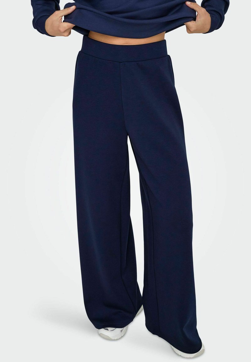 Pantalons de survêtement larges en bleu marine, fabriqués dans un tissu doux, avec une taille haute et une coupe décontractée. Texture lisse sans motifs ni accents visibles.