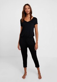 Schwarzer Jumpsuit mit kurzen Ärmeln, V-Ausschnitt und elastischem Bund. Weicher Stoff, verkürzte Länge, minimalistisches Design, keine sichtbaren Muster oder Verzierungen.