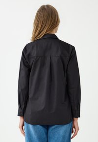 Zwarte shirt met een kraag, zachte stof, lange mouwen en knoopmanchetten. Heeft een rechte achterkant en een ontspannen pasvorm.
