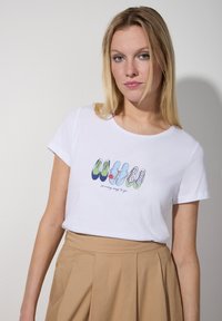 Weißes Baumwoll-T-Shirt mit einem bunten Grafikdesign von Schuhen in unterschiedlichen Mustern und dem Text "so viele Wege zu gehen". Kurze Ärmel, klassische Passform.