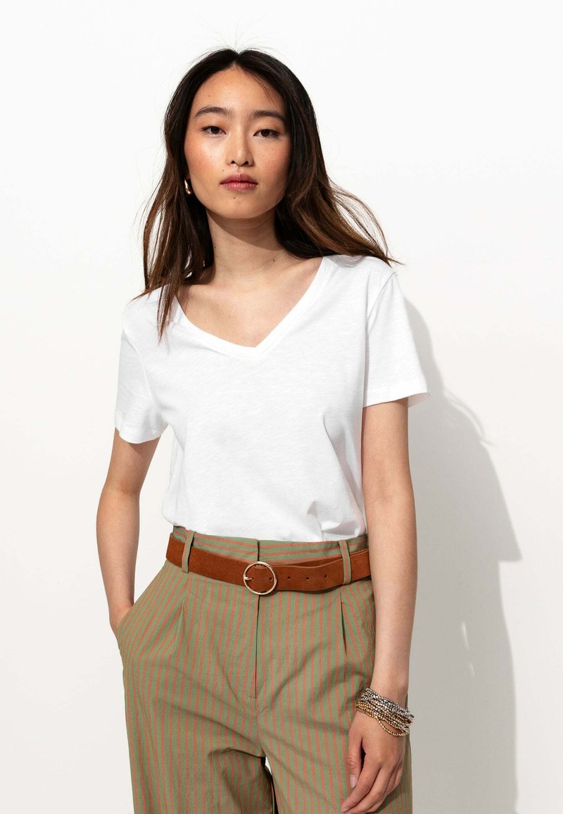 T-shirt blanc à col en V associé à un pantalon taille haute à rayures vertes et une ceinture marron. La tenue présente des manches courtes et une coupe décontractée.