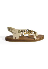 Leren sandalen in beige met kruisende banden, een bruine zool en decoratieve elementen, waaronder kralen en metalen accenten.