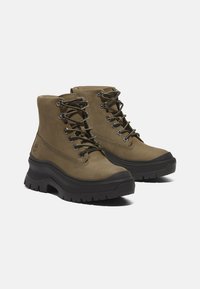 Olive green ankle boots made of leather with a textured surface, featuring black rubber soles, metal eyelets, and contrasting laces.