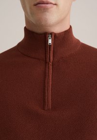 Strickpullover in tiefrostiger Farbe mit hohem Kragen und Viertelreißverschluss. Strukturierter Stoff mit einem subtilen Muster.