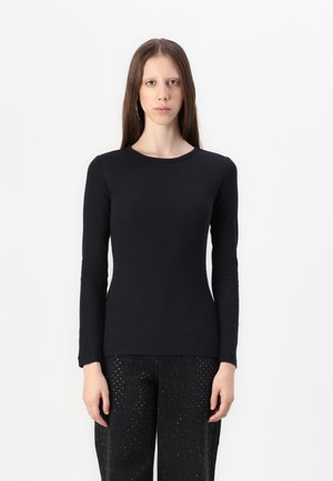 Svart långärmad topp med ribbat mönster, rund halsringning och figurnära design, ihop med mörka, nitarprydda byxor.