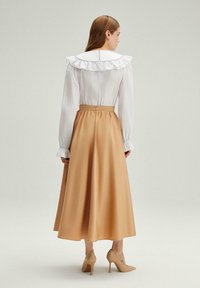 Blusa blanca con cuello con volantes y mangas largas, combinada con una falda larga de satén color marrón claro y tacones altos beige.