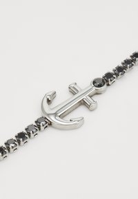 Bracciale in tonalità argento con charm a forma di ancora, arricchito da accenti in pietra nera lungo la catena, creando un design elegante e moderno.