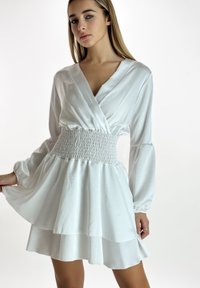 Witte jurk van glad satijnmateriaal, met een geplooide taille, lange pofmouwen en een gelaagde rok.