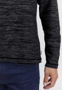 Schwarz- und grau gestreiftes Langarmshirt aus strukturiertem Stoff. Verfügt über einen abgerundeten Saum und ein kleines Markenetikett an der Seite.