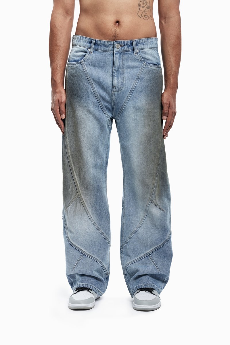 Lichtblauwe oversized denim jeans met een unieke hoekige uitstraling, vervaagde gebieden en contrasterende stiksels, gecombineerd met grijze sneakers.