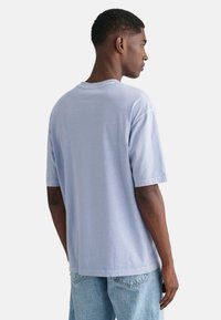 Světle modré bavlněné tričko s krátkým rukávem, uvolněným střihem a kulatým výstřihem. Zadní strana má jednoduchý design s rovný lem.