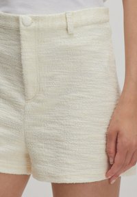Witte textuurshorts met een hoge taille, knoopsluiting en een gladde stof. Het materiaal heeft een licht verhoogd patroon en een nette zoom.