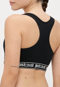 Soutien-gorge noir à dos nageur avec une texture lisse et une bande élastique arborant le logo blanc "Just Cavalli". Design simple, sans motifs supplémentaires.