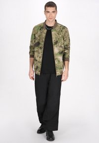 Kamouflage bomberjacka i gröna och beige nyanser, dragkedja, ribbade manschetter, kombinerad med svarta vida byxor och svarta skor.