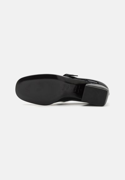 Zapato de charol negro con punta cuadrada, tacón bajo y superficie texturizada. Presenta una correa ajustable para el cierre.