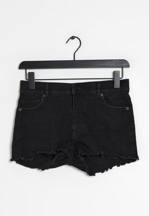 Pantalones cortos de mezclilla negra con dobladillo deshilachado, diseño de cinco bolsillos, cierre de botón de metal y trabillas para cinturón, colgados en una percha negra.