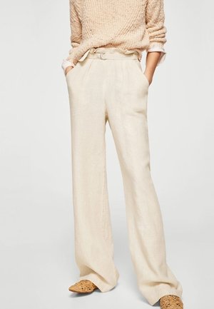 Pantalons larges en lin beige avec des plis avant, taille haute et poches latérales. Associés à un pull en tricot léger et des chaussures tressées.