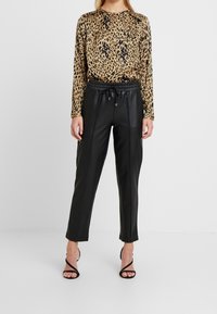 Maglietta a maniche lunghe con stampa leopardata in beige e nero, abbinata a pantaloni tapered neri in similpelle e tacchi alti neri con cinturini.