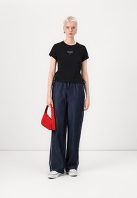 Svart kortermet t-skjorte med røde broderte detaljer, kombinert med løstsittende mørke denimbukser og en liten rød veske. Hvite joggesko.