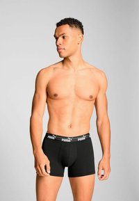 Black boxer briefs with a logo waistband, made of a smooth fabric. The design features a fitted shape and a mid-thigh length.