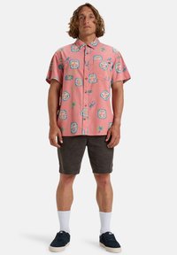 Korte mouw roze shirt met kleurrijke grafische patronen, knopen aan de voorkant en een borstzak, gecombineerd met donkere shorts en sneakers.