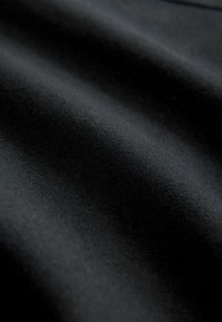 Mustaa kangasta, jossa on sileä, hieman teksturoitu pinta, ja joka sisältää poimuja ja laskoksia, jotka luovat valo- ja varjovaihteluita.