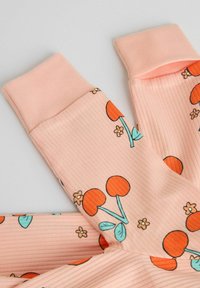Tissu côtelé rose clair avec des imprimés de cerises orange et de petites fleurs sur des jambes de pantalon pliées avec des poignets unis roses.