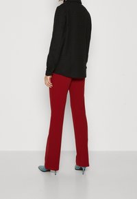 Zwarte gestructureerde jas met lange mouwen, gecombineerd met strakke rode broek. Draagt het met lichtblauwe stilettohakken. De achtergrond is eenvoudig wit.