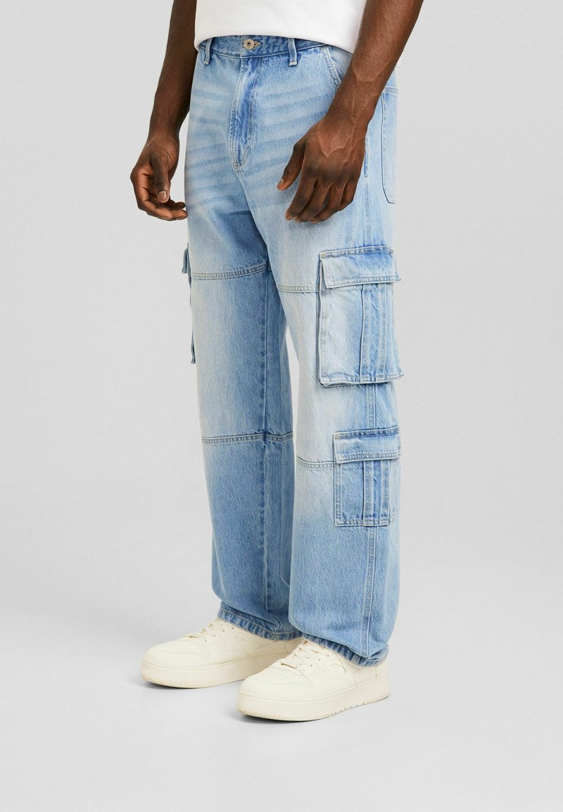 Ljusblå cargobyxor i denim med flera sidofickor, en avslappnad passform och synliga sömmar. Stylade med vita sneakers.