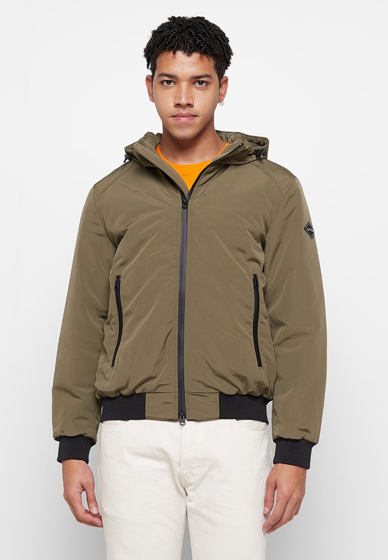 Giacca con cappuccio verde oliva con zip frontale. Presenta due tasche laterali con zip e polsini e orlo a costine neri. Tessuto liscio e leggero.