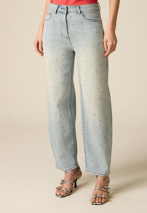 Jean large bleu clair avec de petits strass dispersés, porté avec des sandales à talons fines à motifs noirs et blancs.